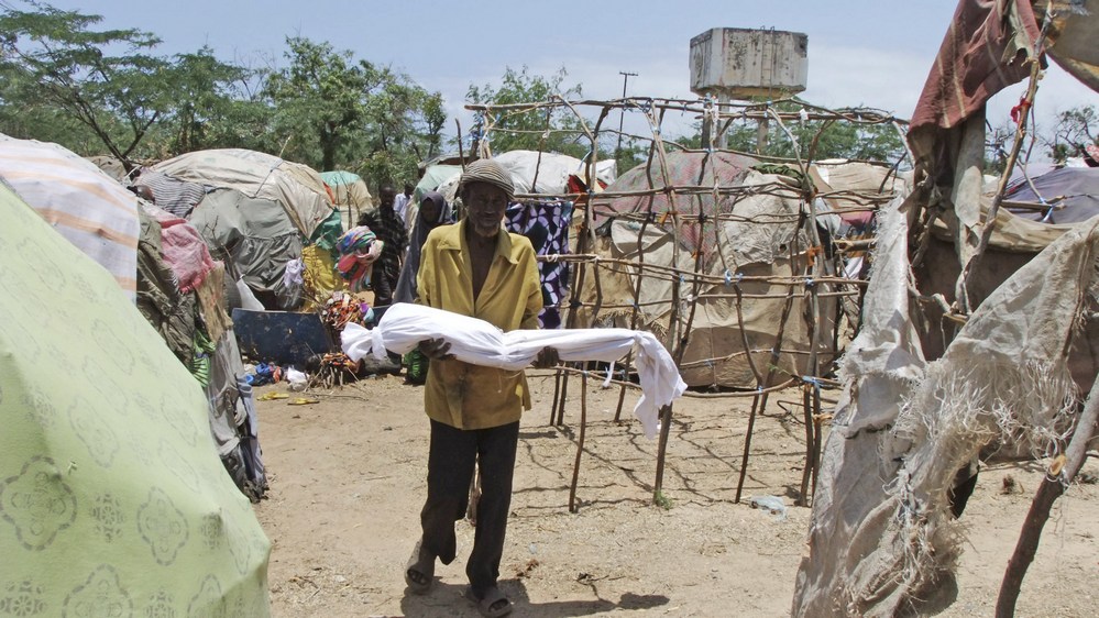 Um homem carrega seu filho morto em um campo de refugiados que acolhe os que escapam da fome, da seca e da guerra em Mogadíscio, na Somália.