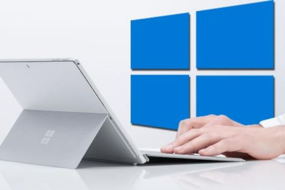 Pessoa utilizando um tablet com a logo do windows 10 atrás